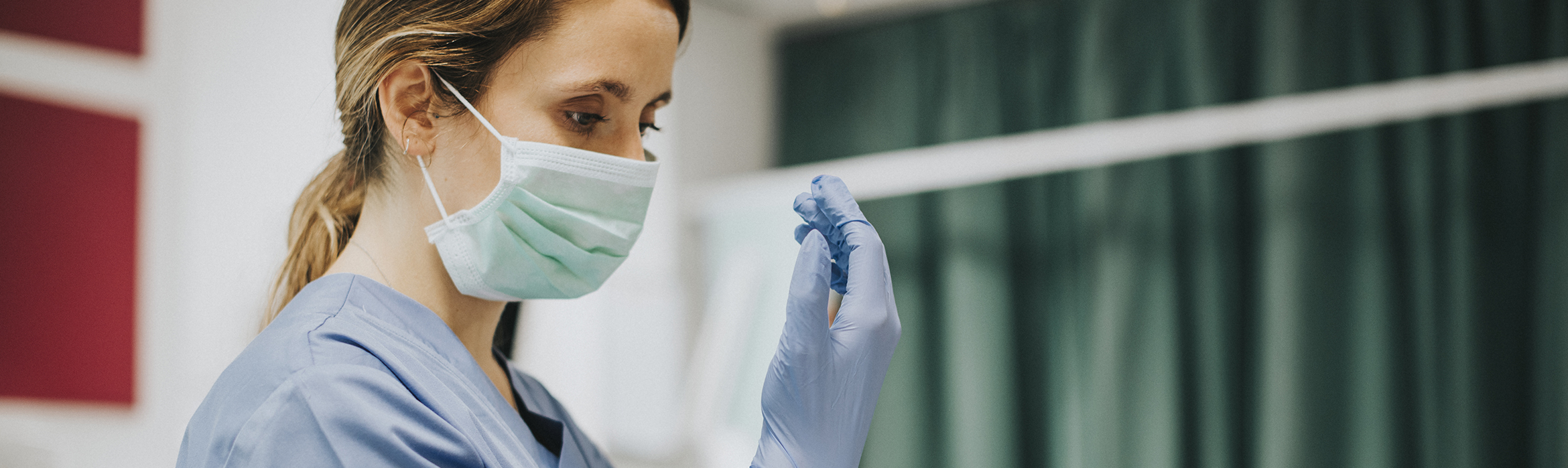 Enfermera con mascarilla y traje azul colocandose un guante